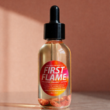 Bottle of 'First Flame' with a dropper on a reflective surface and brown background