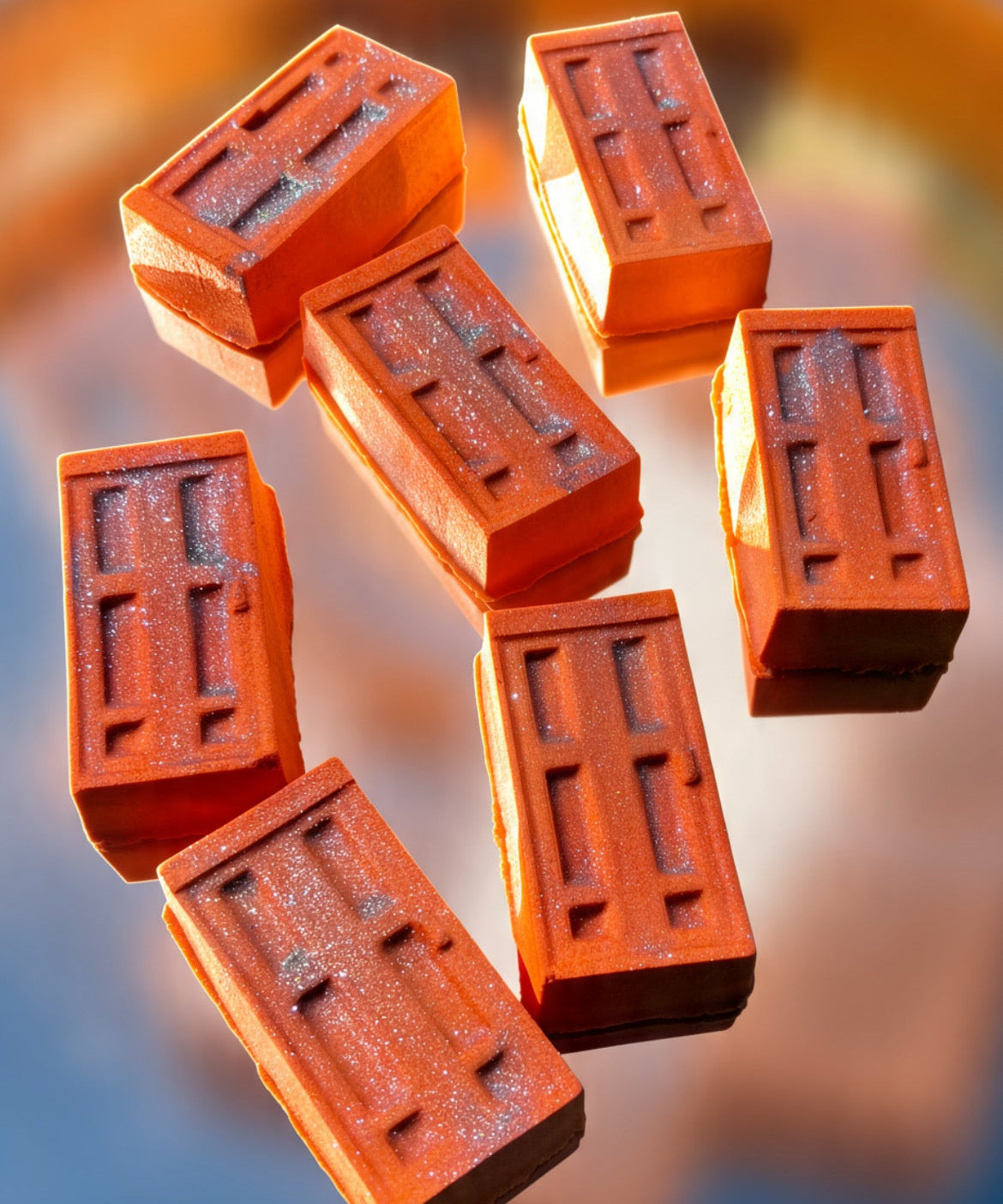 Seven rectangular terracotta-colored blocks with embossed rectangular patterns, arranged in a floating composition against a blurred blue and orange background.