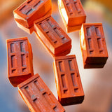 Seven rectangular terracotta-colored blocks with embossed rectangular patterns, arranged in a floating composition against a blurred blue and orange background.