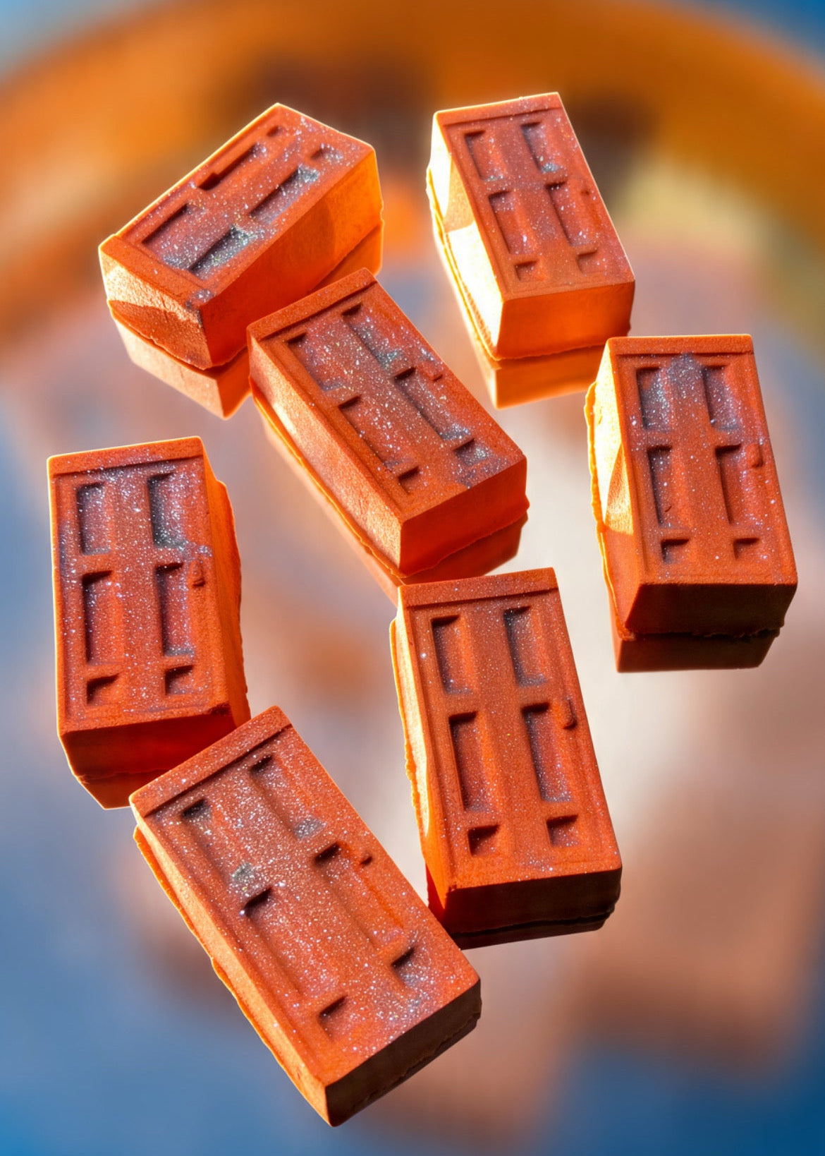 Seven rectangular terracotta-colored blocks with embossed rectangular patterns, arranged in a floating composition against a blurred blue and orange background.