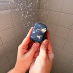 Person holding a small black device with a screen in front of a shower curtain.