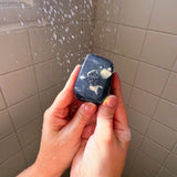 Person holding a small black device with a screen in front of a shower curtain.