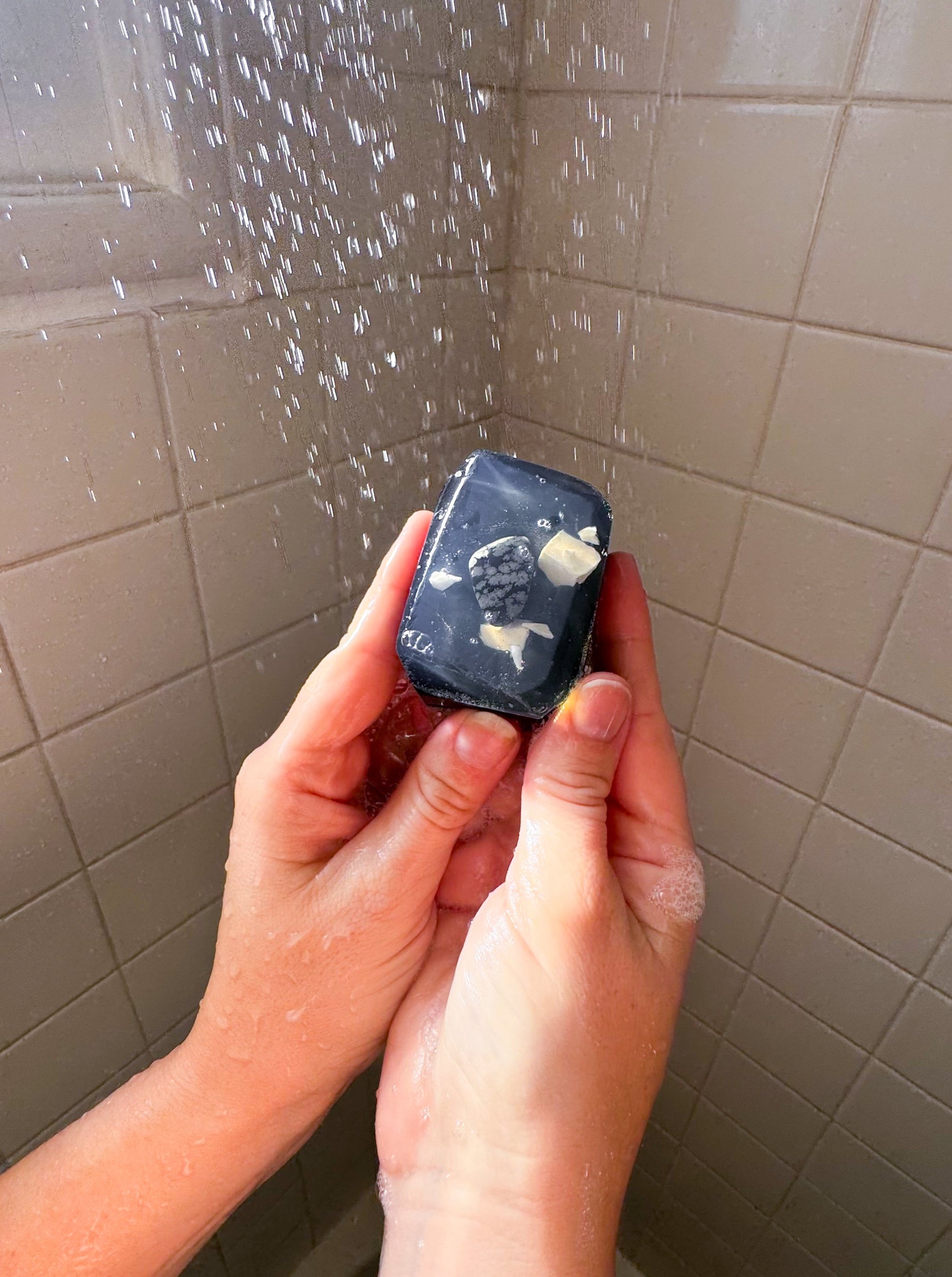 Person holding a small black device with a screen in front of a shower curtain.